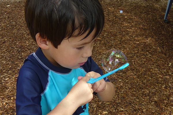 child outside blowing bubbles